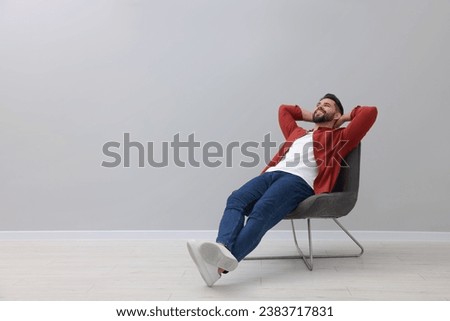 Handsome man relaxing in armchair near light grey wall indoors, space for text