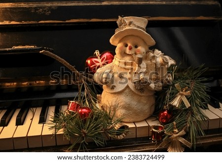 Decorative figurine of a snowman in a hat with a pine branch decorated with Christmas balls and bells on a old shabby piano. Festive new year decor, warm dark composition