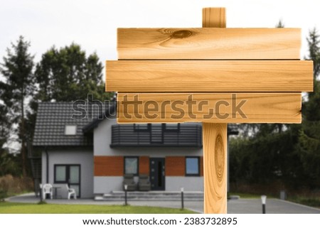 Empty wooden sign near beautiful house outdoors