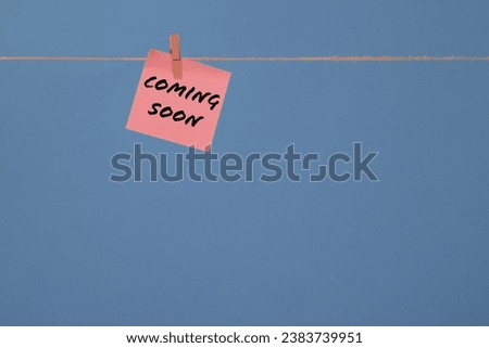 Words coming soon written on pink memo sticky paper and isolated on blue background representing announcements of new project with copy space for text or logo. 