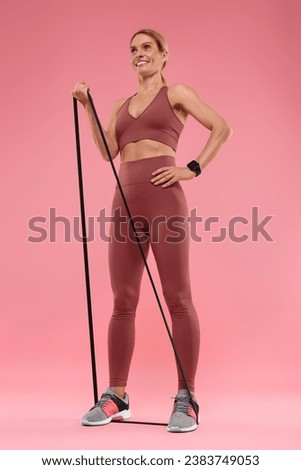 Woman exercising with elastic resistance band on pink background, low angle view