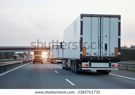Modern white semi-trailer trucks on the highway driving in the right lane. Commercial vehicle for shipping and post delivery. Shipping of the goods on land with a door-to-door delivery process. Royalty-Free Stock Photo #2383761735