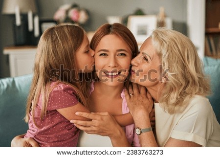 Little daughter and grandmother kissing, embracing young mother at home