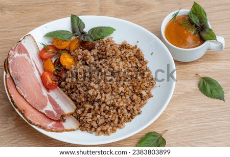 A plate of oatmeal kasha with sausage decorated with leaf and cup of sauce