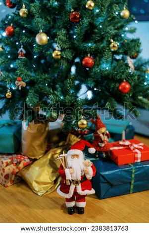 Santa figurine stands near colorful gifts lying on the floor under the Christmas tree