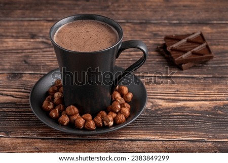 Hazelnut hot chocolate with chocolate next to it on wooden table