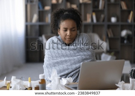 Frustrated ill young Black woman, remote employee, patient wrapped in warm plaid suffering from cold, fever, flu, influenza, taking pills, making video call, consulting doctor online, using laptop Royalty-Free Stock Photo #2383849837