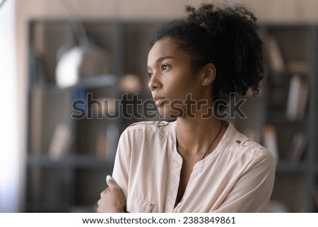 Thoughtful millennial African American girl, student, young woman looking at window away in deep thoughts, thinking over challenges, difficult tasks, feeling bored, sad. Head shot portrait Royalty-Free Stock Photo #2383849861