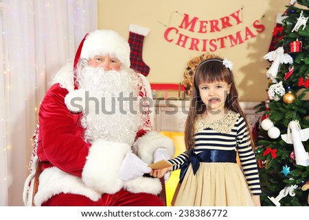 Little cute girl giving letter with wishes to Santa Claus near Christmas tree at home