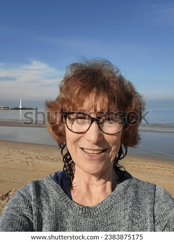Mature woman takes a sunny winter selfie after cold water swim at St Kilda Beach. Open or cold water therapy in the sea is known to have benefits for physical and mental health.