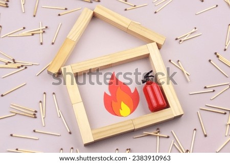 A box of matches placed next to a toy red fire extinguisher against a light background. Fire safety concept. International Firefighter's Day.