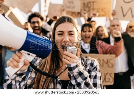 Large group of diverse people manifesting against war or attack on a country. Female activist using megaphone outdoors. Stop war signs and banners in a peace demonstration Royalty-Free Stock Photo #2383920565