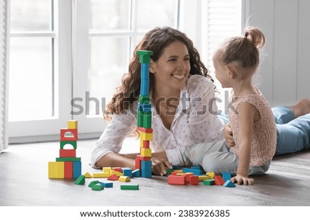 Beautiful loving mother play wooden cubes with cute little daughter, spend time on warm floor enjoy playtime, family leisure and developmental games at cozy home. Babysitting, upbringing, motherhood Royalty-Free Stock Photo #2383926385