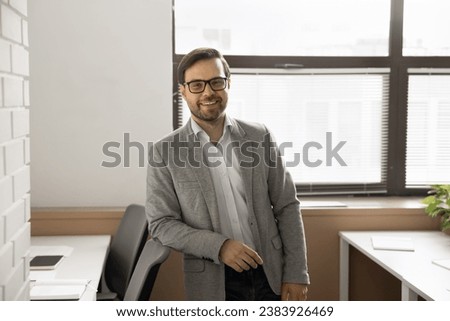 Relaxed positive handsome businessman in formal clothes and glasses looking at camera, smiling, laughing, leaning on office chair. Successful executive, director, CEO, company owner portrait