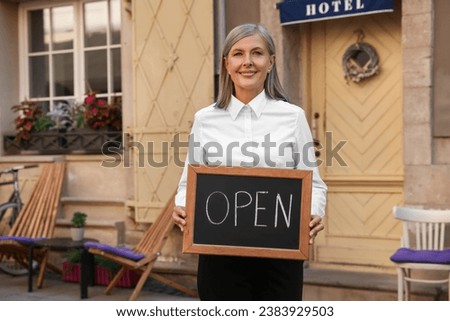 Happy business owner holding open sign near her hotel outdoors