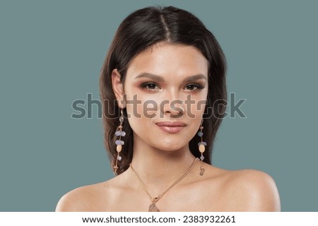 Pretty young adult glamorous woman with shiny clear skin wearing jewelry golden necklace and long earring with blue and white amethyst and opal, fashion studio portrait closeup