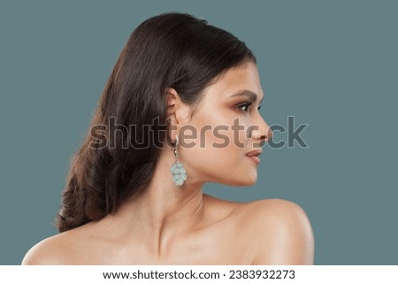 Pretty stylish lady portrait. Brunette woman in gold jewelry earring posing on blue background