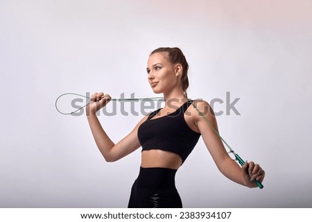 Young female fitness trainer in black sports uniform posing with skipping rope holding on shoulders. Street training of young cute female athlete jumping rope Royalty-Free Stock Photo #2383934107
