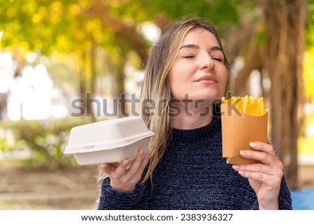 Young pretty Romanian woman holding burger and chips at outdoors