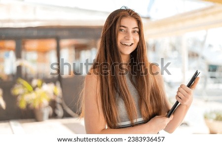 Young pretty caucasian woman holding a tablet at outdoors smiling a lot
