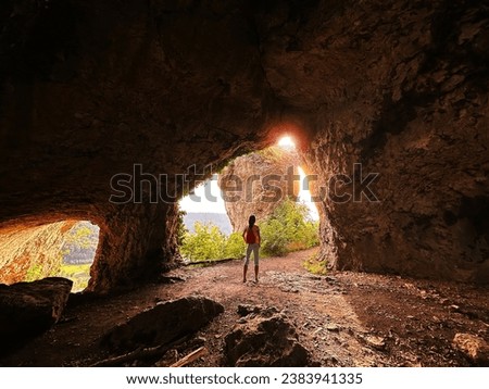 Tiny Human Silhouette With Red Backpack Enjoying Sunset Light Over The Rock From Inside The Cave With Copy Space For Text Overlay, Amazing View From Inside The Cave To Rocky Picturesque Landscape At S