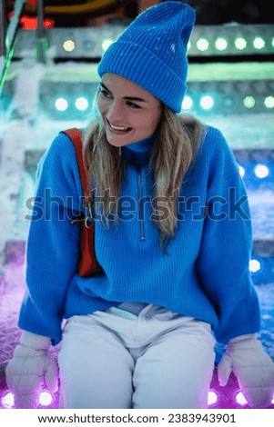 Cheerful and stylish woman, dressed in warm clothes, is having fun in a snowy winter amusement park.