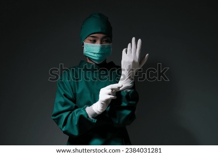 Female doctor surgeon wearing scrub overall suit for medical surgery clothing putting on rubber surgical glove, operation uniform ready to operate on ill patient in operating room, healthcare medical