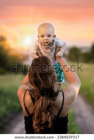 Sunset with a woman holding a small boy above her head. Royalty-Free Stock Photo #2384039317