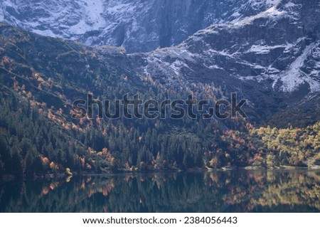 Autumn's Mirror: Vibrant Fall Foliage Reflects in Morskie Oko's Waters, a Perfect Blend of Warm Tones and Snowy Peaks for Idyllic Nature Settings.