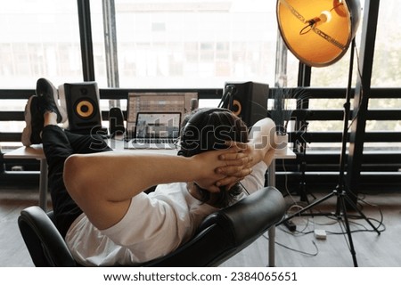 Back view of unrecognizable male musician sitting at table with loudspeaker enclosure near panoramic window and composing music Royalty-Free Stock Photo #2384065651