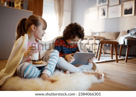 Little boy using tablet with his sister on living room floor Royalty-Free Stock Photo #2384066301