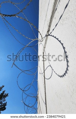 Barbed wire on white wall and blue sky with shadows from bright sun. High quality photo