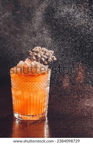 Professional male bartender spraying on the delicious transparent red cocktail in the glass on the bar counter in the blurred background