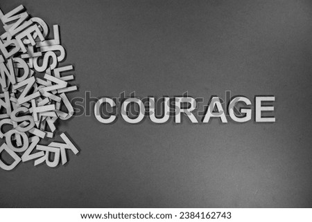 Courage in wooden English language capital letters spelling positive opinion spilling from a pile of letters in black and white