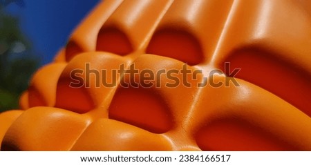 Orange yoga roller in the sun in a clear blue sky; blurred silhouette of treetops on the left (macro, side view, diagonal, texture).