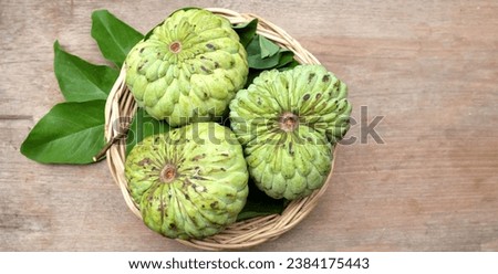 fresh green raw custard apple,sugar apple, annona cherimola (annona squamosa l.) fruit with leaf in a wicker basket on a wooden table backdrop. tropical exotic fruit and healthy fruits