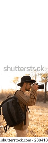Young professional male photographer shooting autumn nature outdoor on modern camera. Vertical banner. Copy space