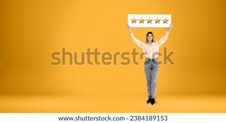 Full length portrait of cheerful young European woman in casual clothes holding five stars sign above her head over yellow copy space background. Concept of product and service evaluation