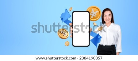 Smiling woman showing mockup smartphone blank screen, gold dollar and yen or yuan coins on empty blue background. Concept of mobile app, money transfer and conversion