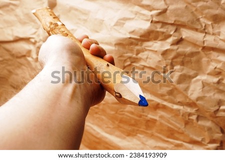 Rough male hand holding a large pencil made of a wooden stick