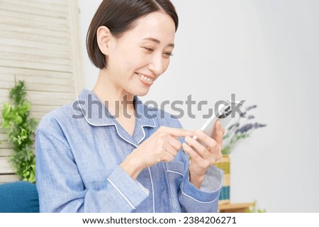 Asian middle aged woman using the smartphone in the living room wearing pajamas