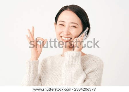 Asian middle aged woman with the smartphone OK gesture in white background