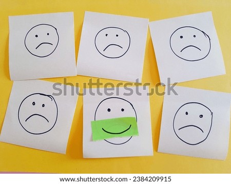 Smile, concept, a smiling face in the middle of five sad faces made of yellow sticky notes on a yellow background, positive motivation, positive note 