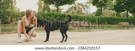 Girl walks along the path in the park with back dog.