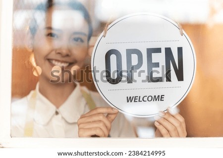 Asian small business owner woman turning shop entrance sign to open on front door entrance happily. Woman hanging open sign on the glass window. Focus on sign.
