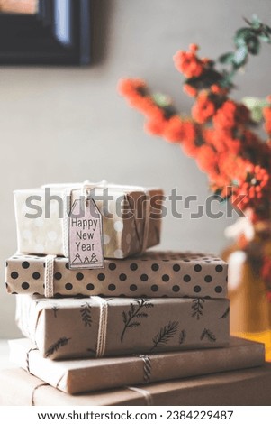 Stack of gift boxes with happy new year gift tag on table. Firetorn branches in vase, picture on the wall