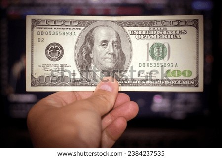 photo of 100 dollars in hand against the background of a monitor with quotes. Darkened background. Business marketing, inflation, finance news