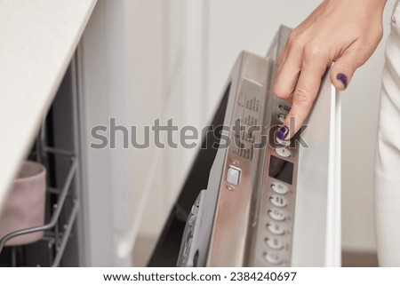 female hand turning on dishwasher machine in kitchen, woman choosing mode program on control panel of dishwasher.