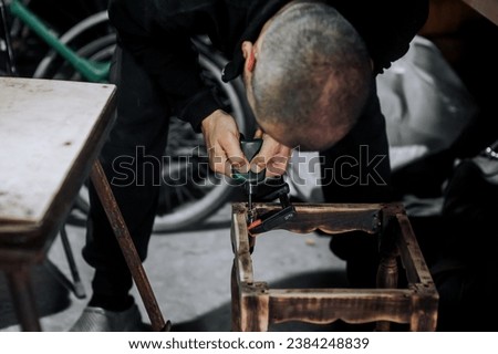 Male professional woodworker carpenter glues a chair, repairs, restores furniture in the workshop, clamping wooden products with a clamp. Photography, work concept, portrait.
