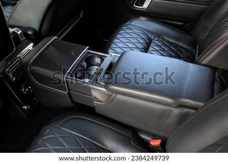 Armrest with table and cup holder in luxury SUV. Black Leather folding armrest with cup holders in rear seats inside a vehicle.  Royalty-Free Stock Photo #2384249739